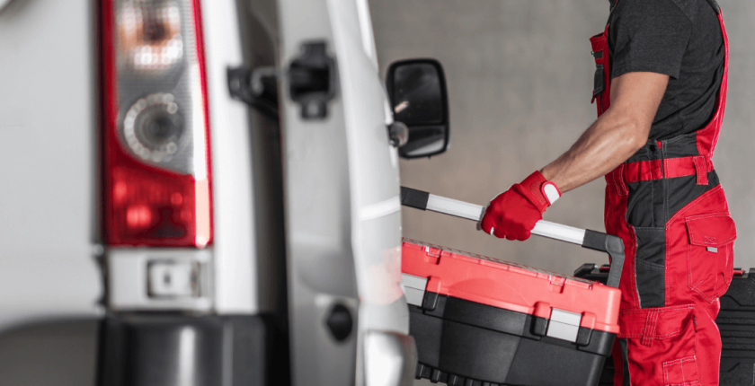 Vehicle technician in red overalls stood next to a commercial van with a toolbox