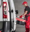 Vehicle technician in red overalls stood next to a commercial van with a toolbox